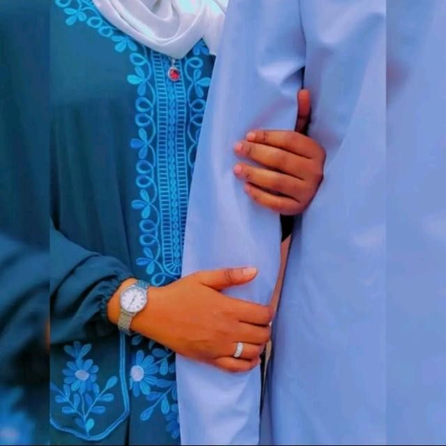 يدا امرأة وخاتم الزواج في إصبعها على ذراع زوجها بلباس تقليدي