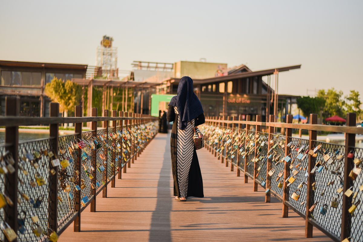 امرأة محجّبة تبتعد على جسر خشبي تغطّي الأقفال حواجزه